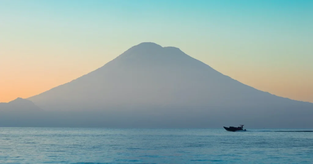 A boat passes in front of the volcanoes in Lake Atitlan during sunrise