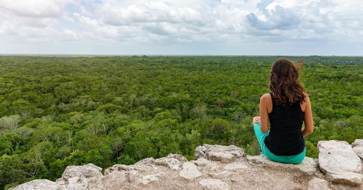 A girl is sitting in the tallest pyramid of Coba the Nohoch Mul and looking at the jungle canopy below