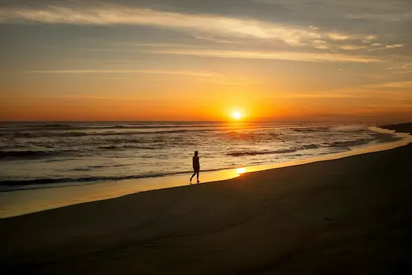 A woman is walking in the black sand beach of El Paredon during sunset