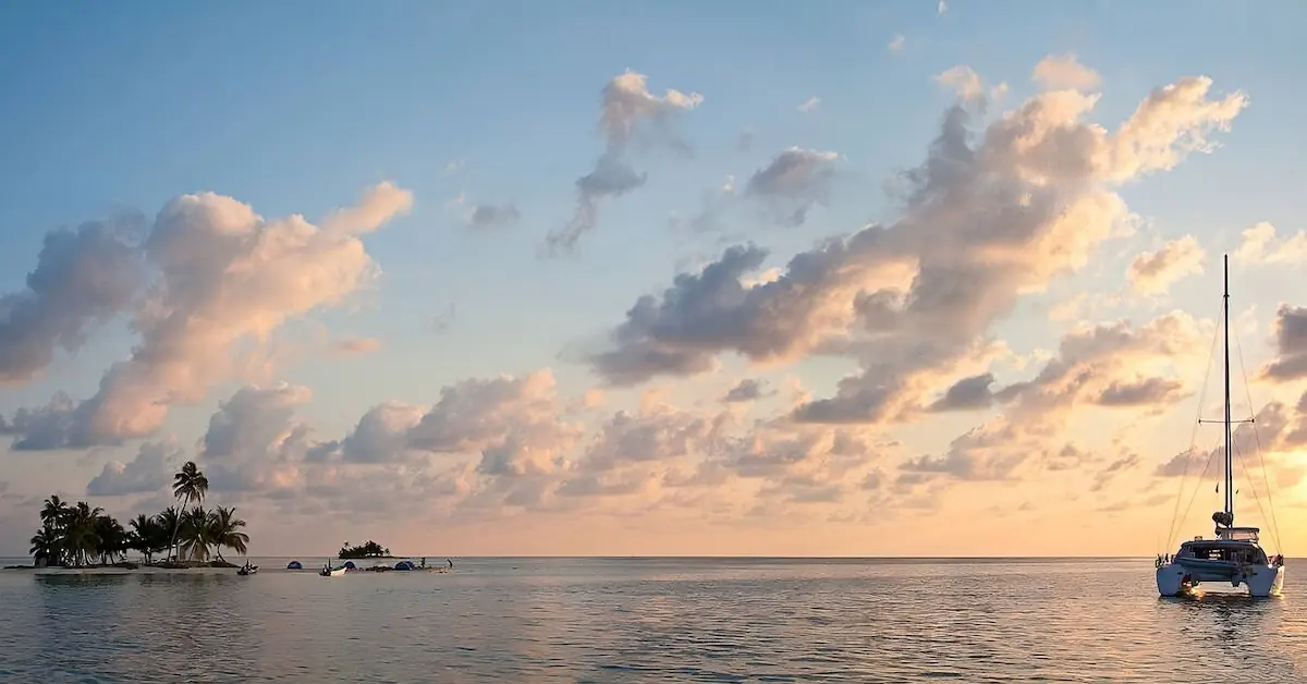A Catamaran is next to the little island of Queen Caye in the Caribbean Ocean during sunset