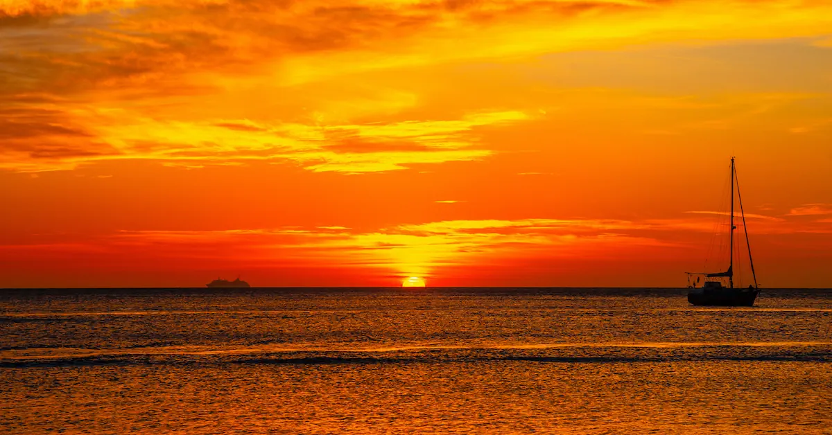 A sailing boat anchored in the calm ocean waters off the tropical coast of Roatan at sunset.
