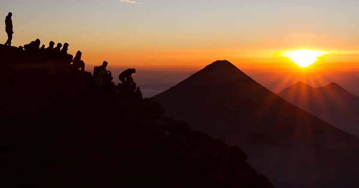 A group observes the sunrise over the volcano de Agua from volcano Acatenango during an overnight hike