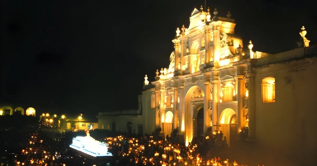 A procession is passing in front of the Cathedral of Antigua Guatemala while people are holding candles
