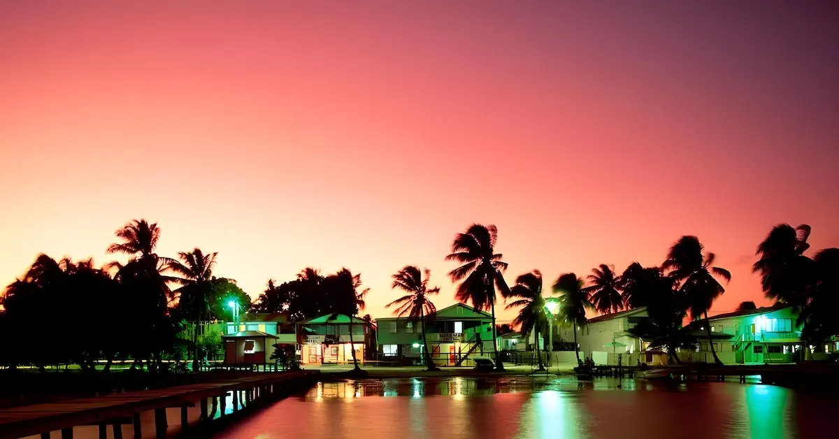 The shoreline of Caye Caulker with palm trees and houses with lights during twilight
