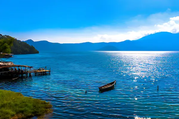 The blue water of Lake Coatepeque and surrounding mountains during a sunny blue sky day