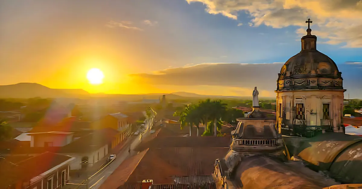 View over Granada, Nicaragua at sunset, featuring colonial tiled roofs and a church dome against the golden sky.
