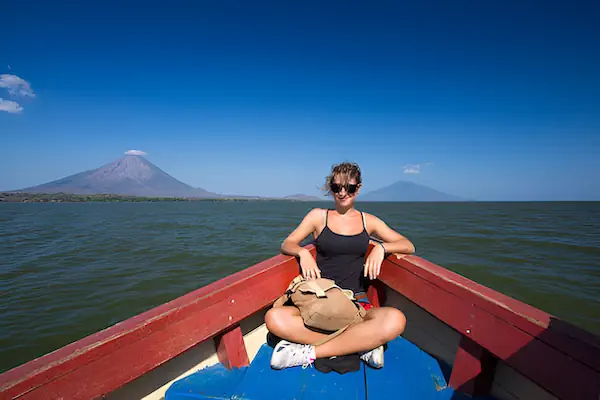 A young woman is sitting on a wooden boat during a sunny day with the two volcanoes of Ometepe Island in the background