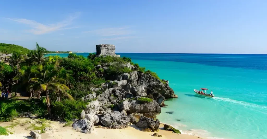 A small motor boat goes through the turquoise waters of the Caribbean in front of the Mayan site of Tulum