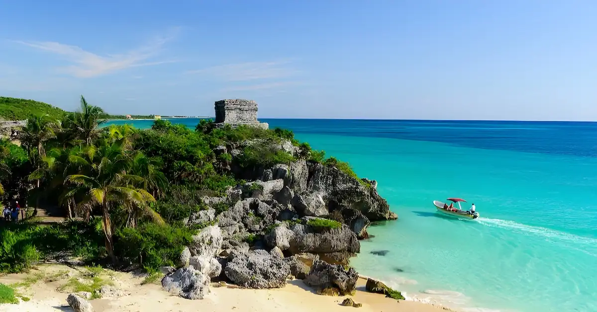 A small motor boat goes through the turquoise waters of the Caribbean in front of the Mayan site of Tulum