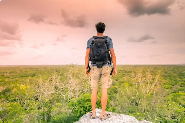 A young man is looking at the endless jungle from the top of one of the pyramids in the Maya ruins of Caracol in Mexico