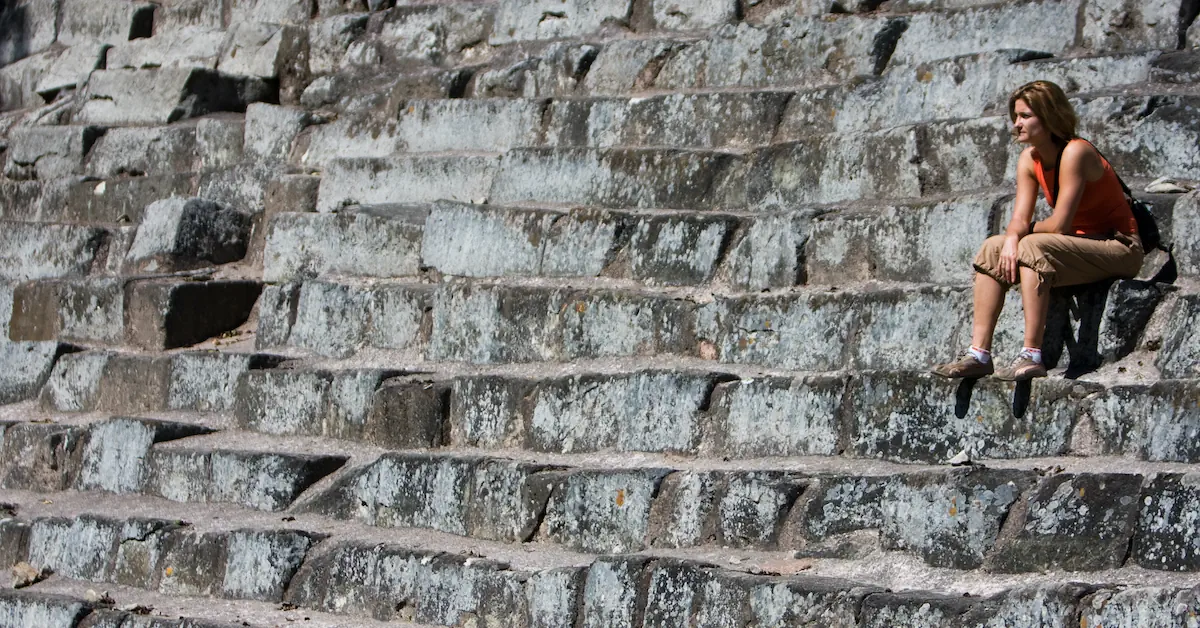 A young woman is sitting on the stairs of a Maya temple in Copan ruins