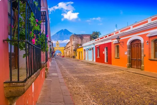 A colorful street in Antigua Guatemala with the Santa Catalina Arc and the Volcano de Agua in the background