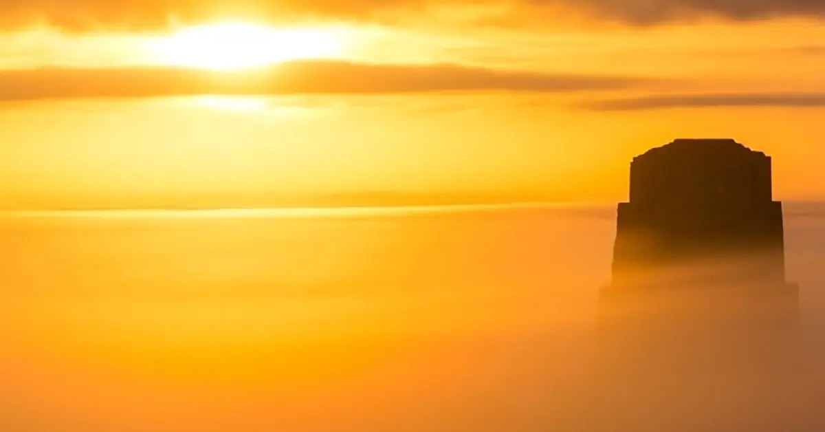 Silhouetted peak of an ancient Mayan temple in Tikal, Guatemala, rising above a sea of glowing golden morning mist.