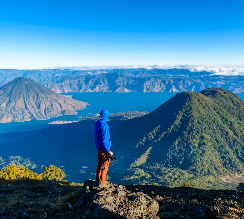 A tourist hiking one of the volcanoes in Lake Atitlan is looking at the other volcanoes and holds a camera on his hand