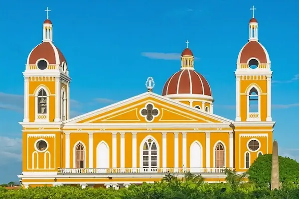 The striking yellow and white colonial architecture of the Granada Cathedral standing against a bright blue sky in Nicaragua.