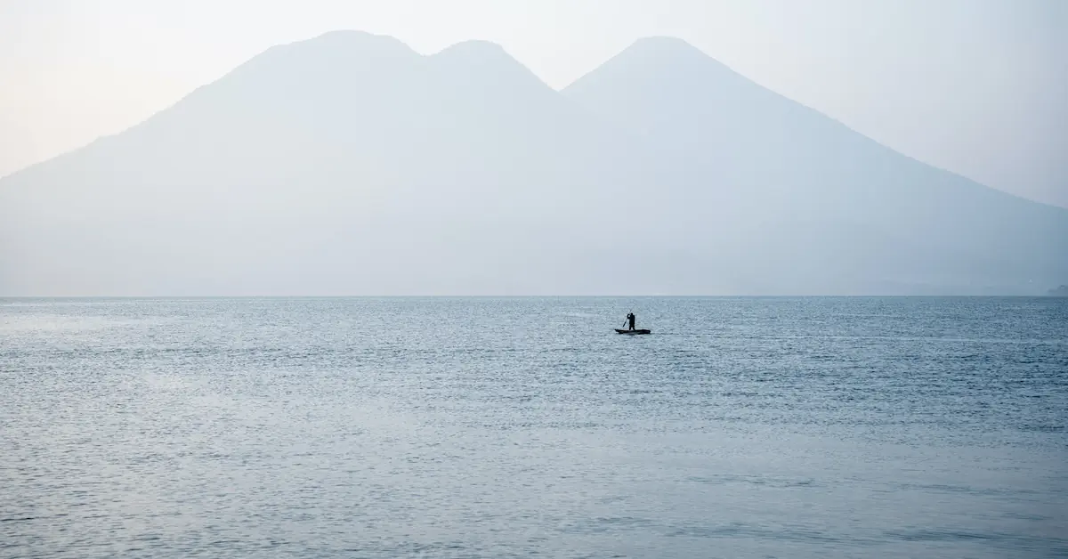 A traditional fisherman is navigating in his wooden canoe with the impossing volcanoes of Lake Atitlan in the background