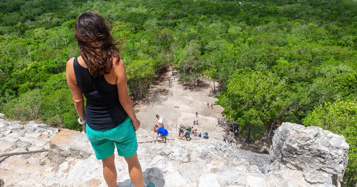 Traveler looks down the steep stone steps of the ancient Coba ruins in Mexico toward the lush green jungle below.
