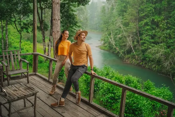 A couple on a wooden deck admires the vibrant turquoise Chijul River and misty forest in Guatemala.