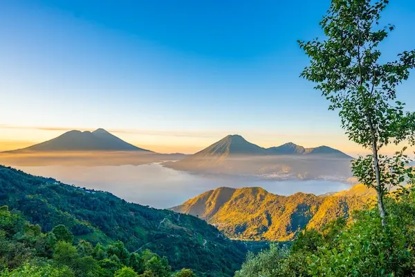Sunrise mist over Lake Atitlán, Guatemala, framing the silhouettes of its three towering volcanoes.