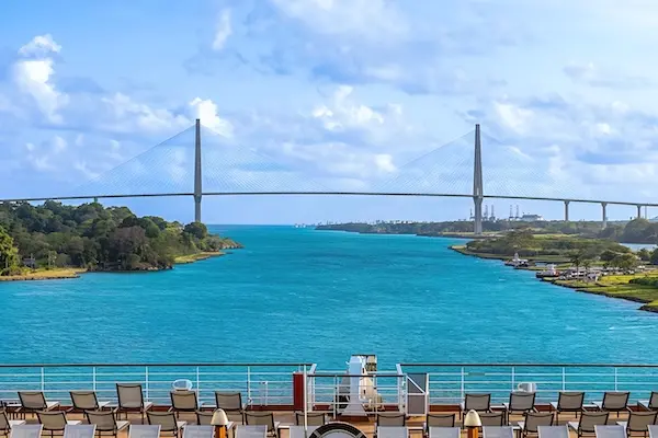 The Atlantic Bridge spanning the Panama Canal, viewed from a cruise ship deck with lounge chairs in the foreground