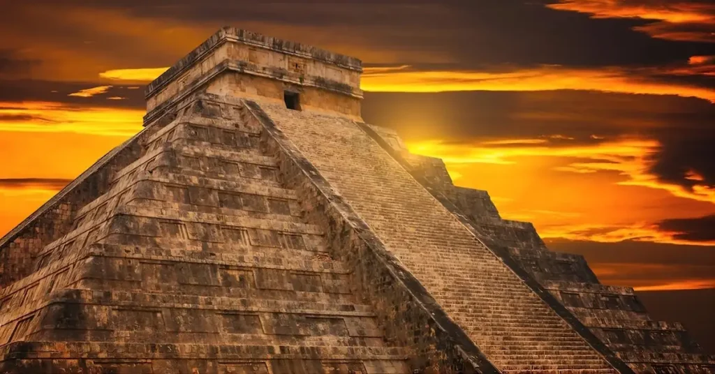 El Castillo stepped stone pyramid at Chichen Itza set against a bright orange sunset sky.
